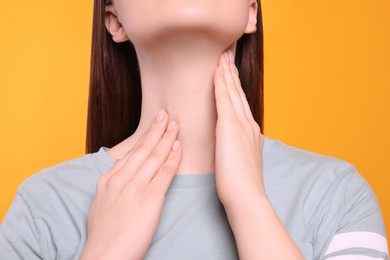 Woman with sore throat on orange background, closeup