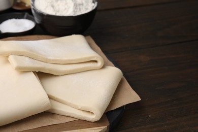 Photo of Raw puff pastry dough on wooden table, closeup. Space for text