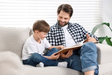 Happy dad and son reading book together on sofa at home