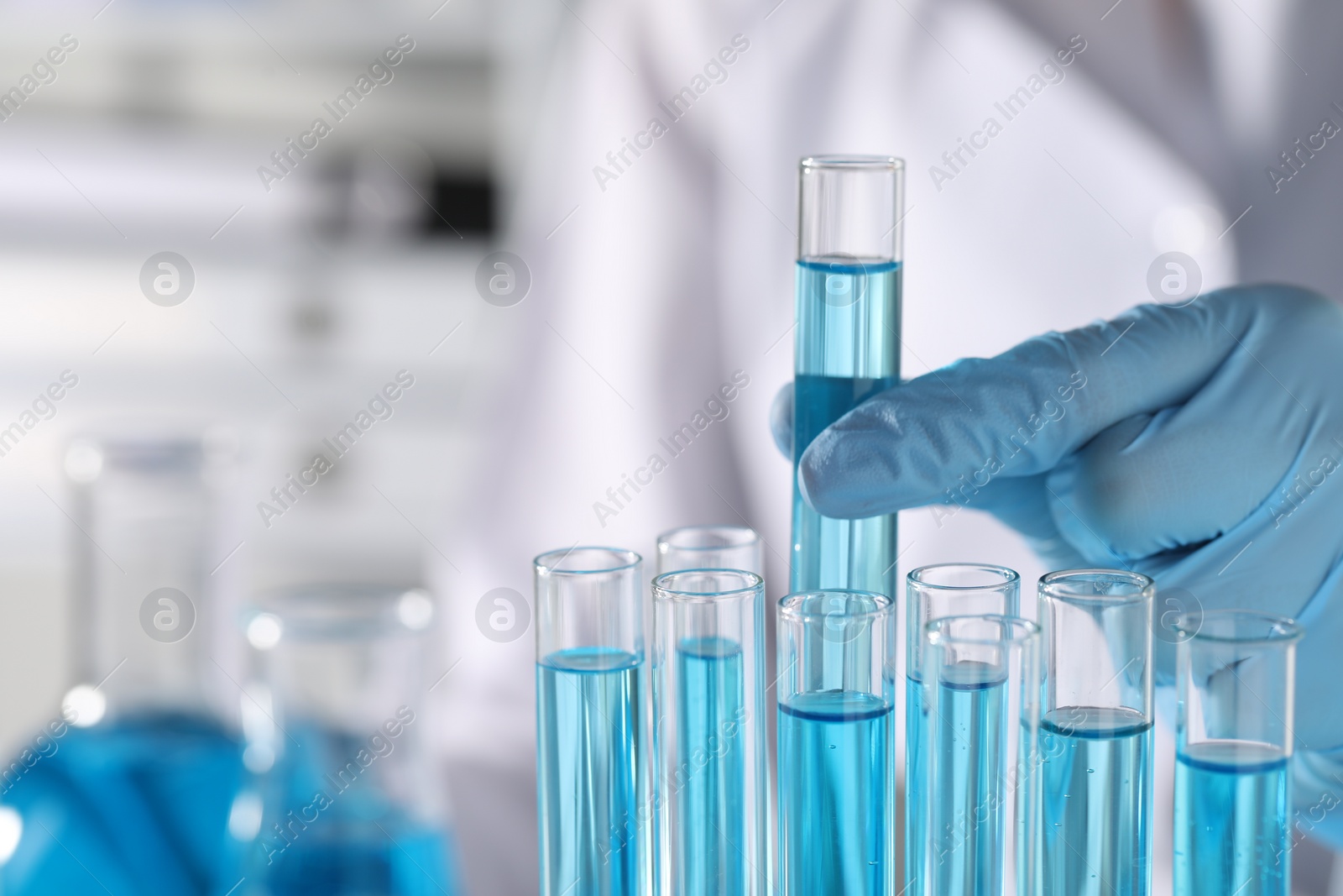 Photo of Scientist taking test tube with light blue liquid in laboratory, closeup. Space for text