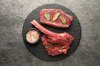 Photo of Pieces of raw beef meat and spices on grey textured table, top view