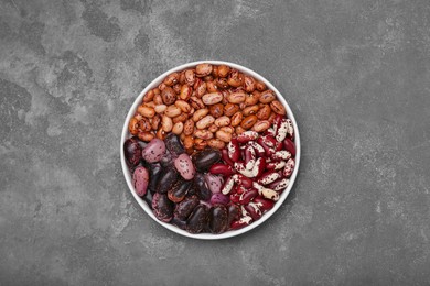 Bowl with different types of beans on grey table, top view