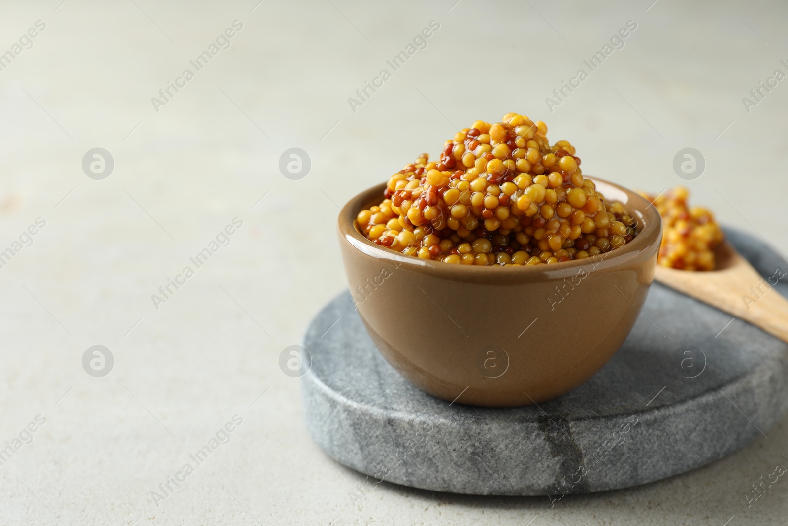 Photo of Fresh whole grain mustard in bowl on white table. Space for text