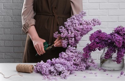 Woman trimming lilac branches with secateurs at white wooden table, closeup