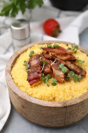 Photo of Cooked cornmeal with bacon and microgreens in bowl on light grey table, closeup