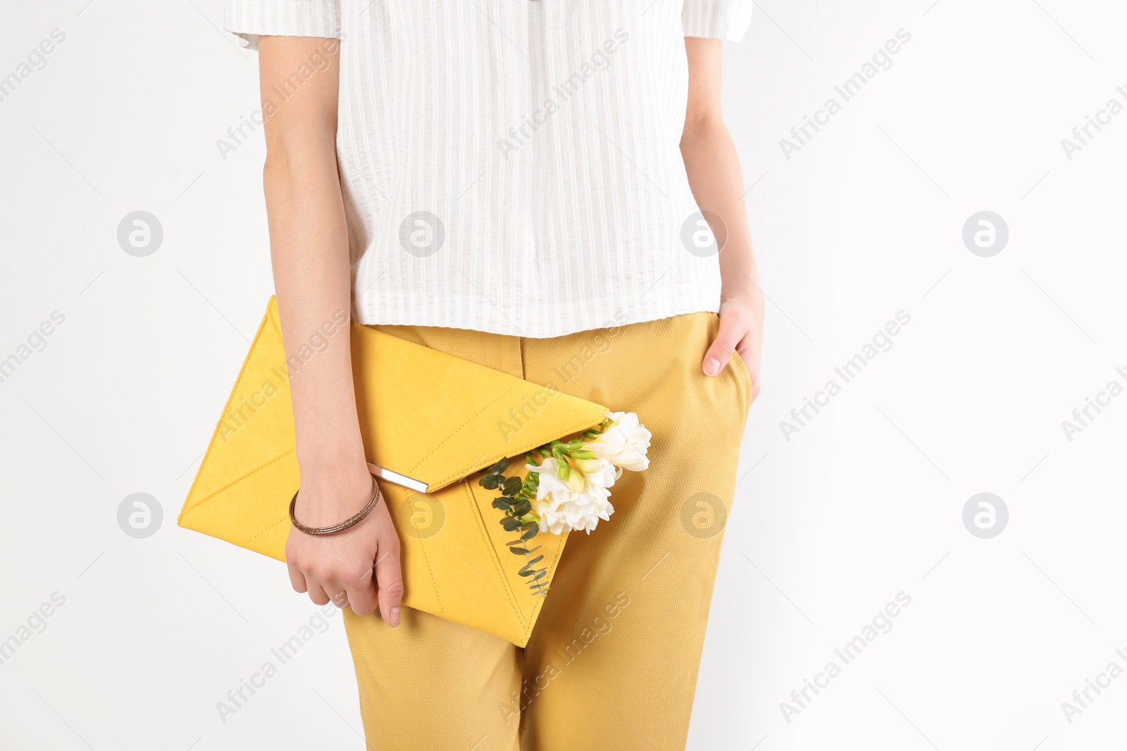 Photo of Stylish woman with clutch and spring flowers against light background, closeup