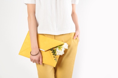 Photo of Stylish woman with clutch and spring flowers against light background, closeup