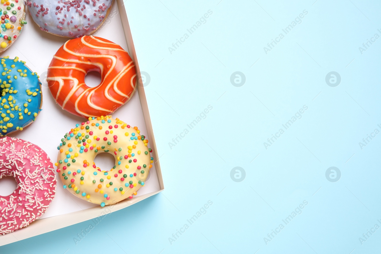 Photo of Delicious glazed donuts on light blue background, top view. Space for text