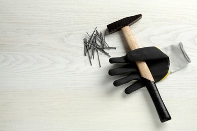 Photo of Hammer, glove and metal nails on white wooden table, flat lay. Space for text