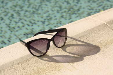 Photo of Stylish sunglasses near outdoor swimming pool on sunny day, space for text