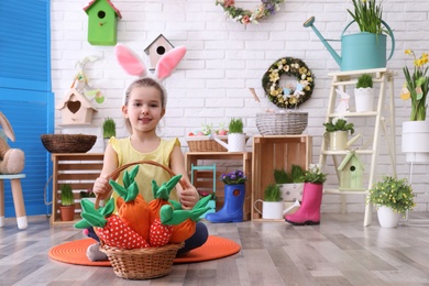 Adorable little girl with bunny ears and basket full of toy carrots in Easter photo zone