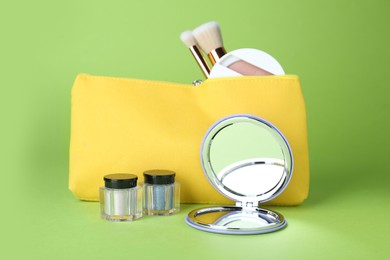 Stylish pocket mirror and cosmetic bag with makeup products on light green background