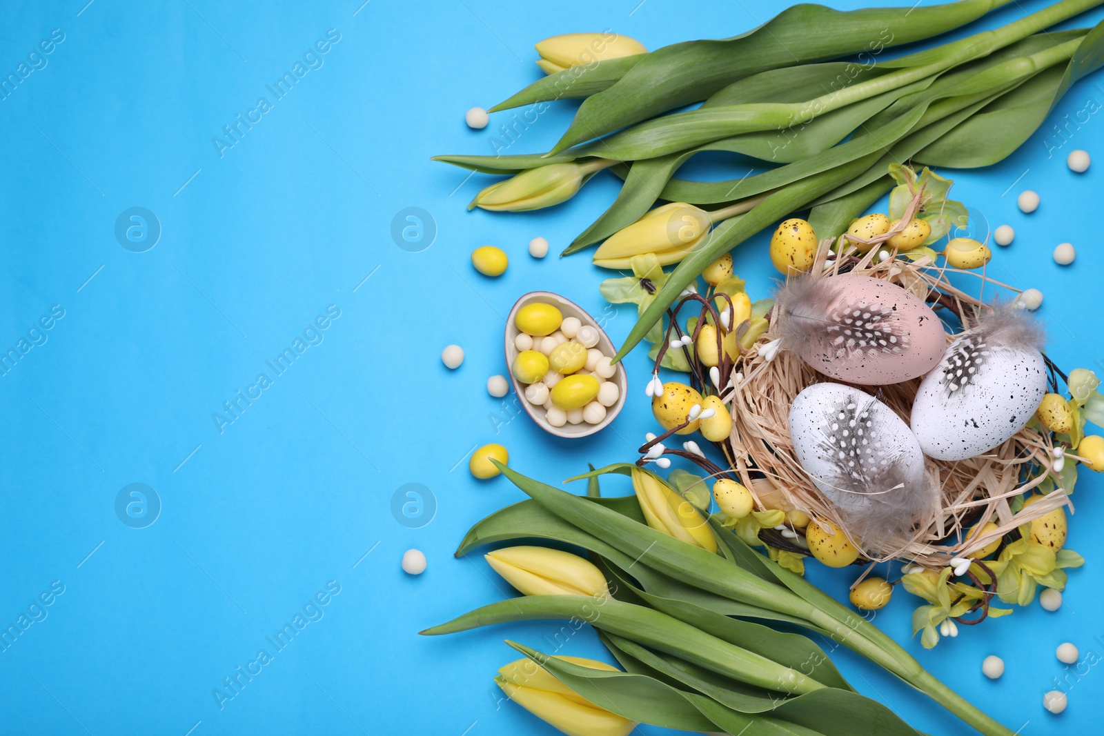 Photo of Flat lay composition with beautiful flowers and eggs on light blue background, space for text. Easter celebration