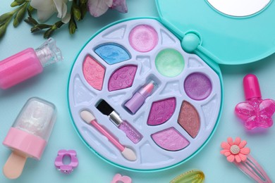 Photo of Decorative cosmetics for kids. Eye shadow palette, lipsticks, accessories and flowers on light blue background, flat lay