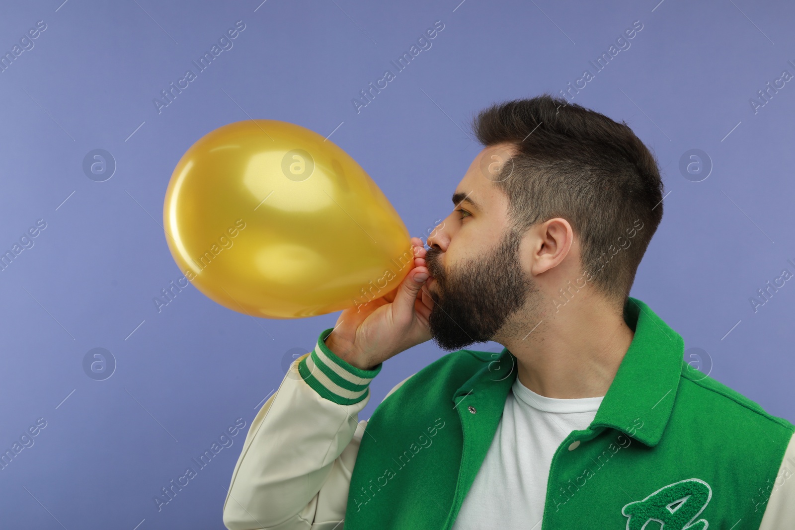 Photo of Man inflating bright balloon on violet background