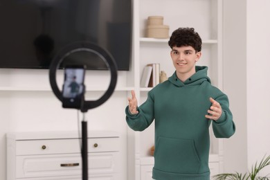 Photo of Smiling teenage blogger explaining something while streaming at home