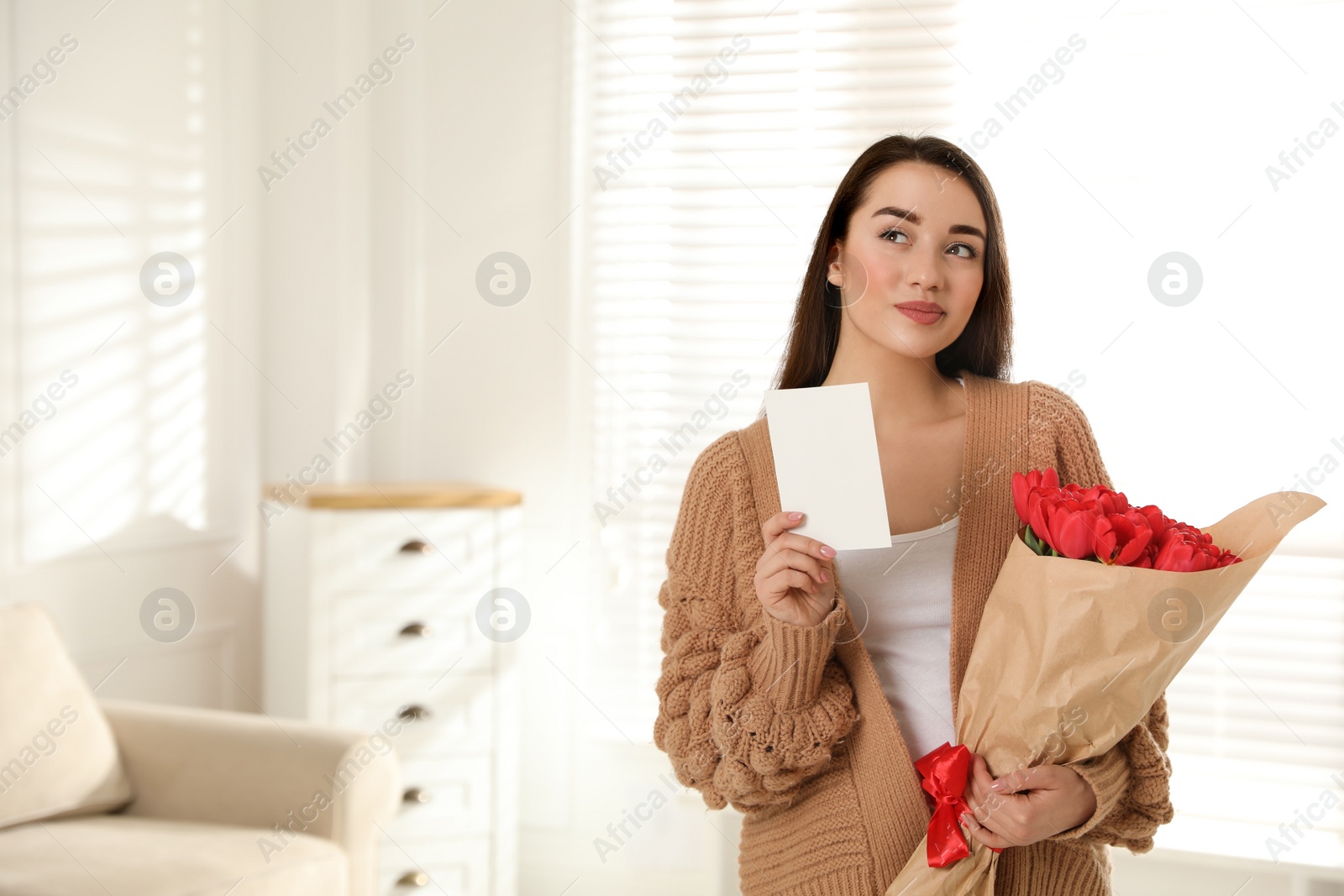 Photo of Happy woman with red tulip bouquet and greeting card at home, space for text. 8th of March celebration