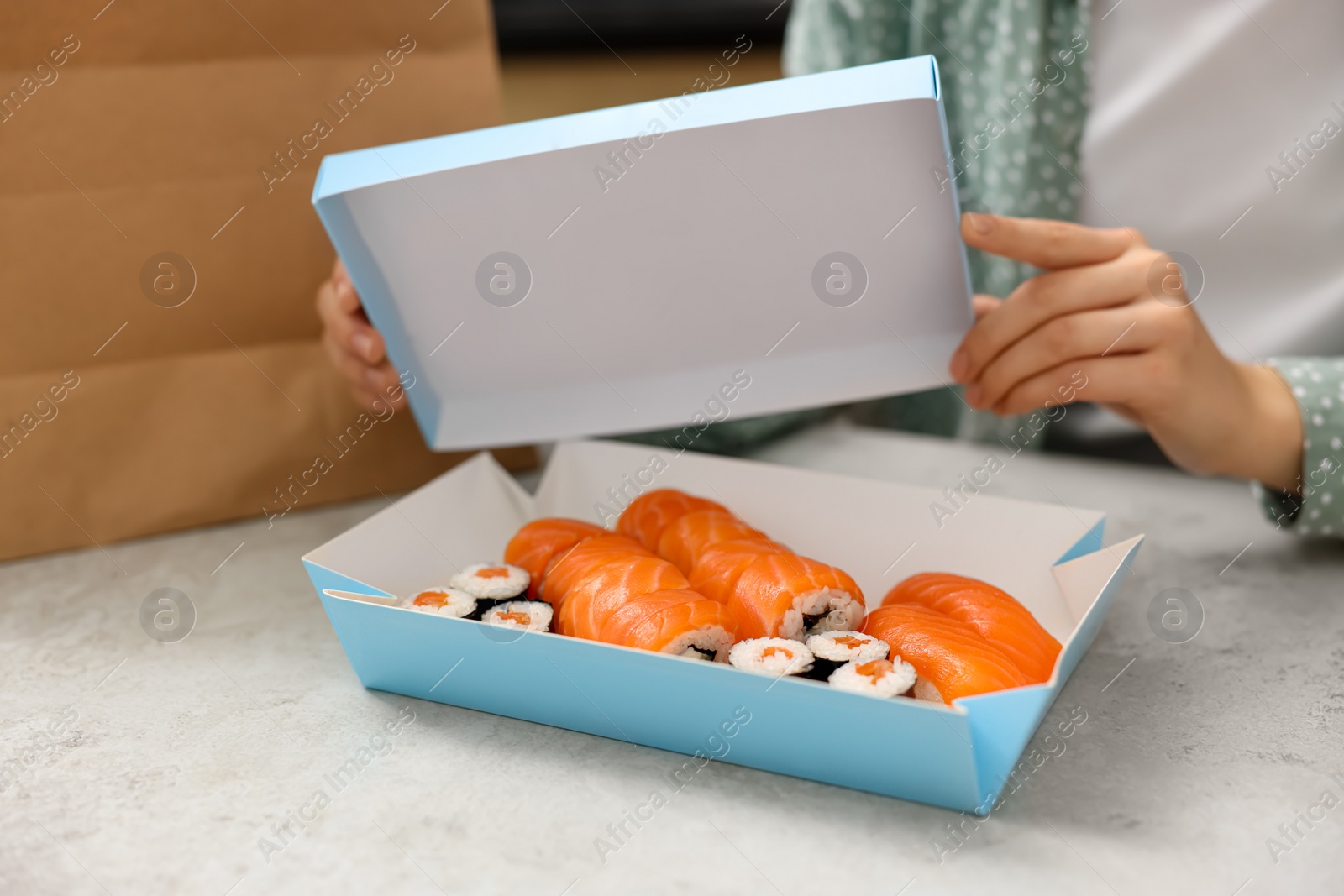 Photo of Woman unpacking her order from sushi restaurant at table in kitchen, closeup