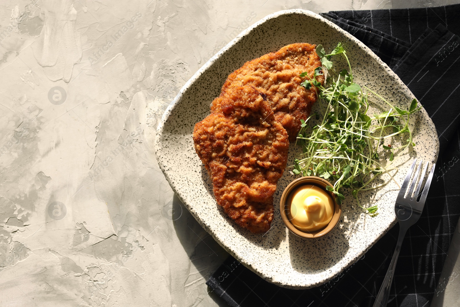 Photo of Tasty schnitzels served with sauce and microgreens on grey textured table, top view. Space for text