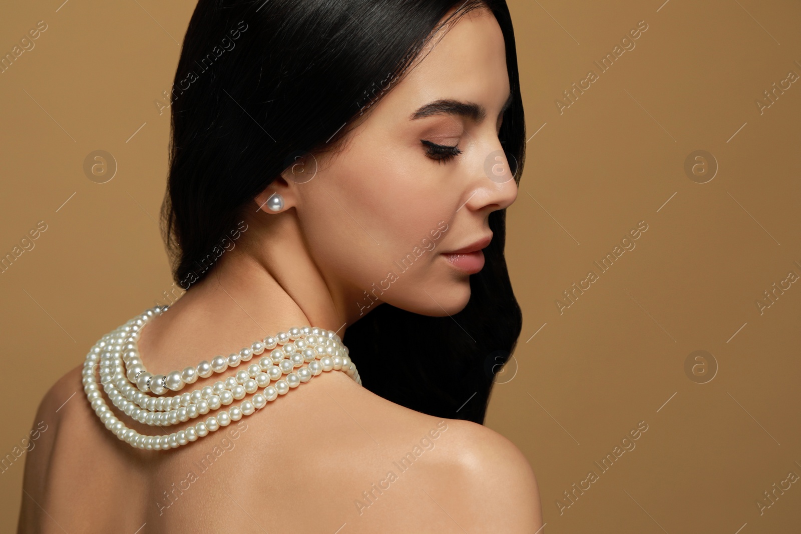 Photo of Young woman wearing elegant pearl jewelry on brown background