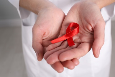 Photo of Woman holding red awareness ribbon indoors, closeup. World AIDS disease day