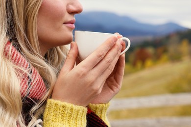 Young woman with cup of hot drink in mountains, closeup. Space for text