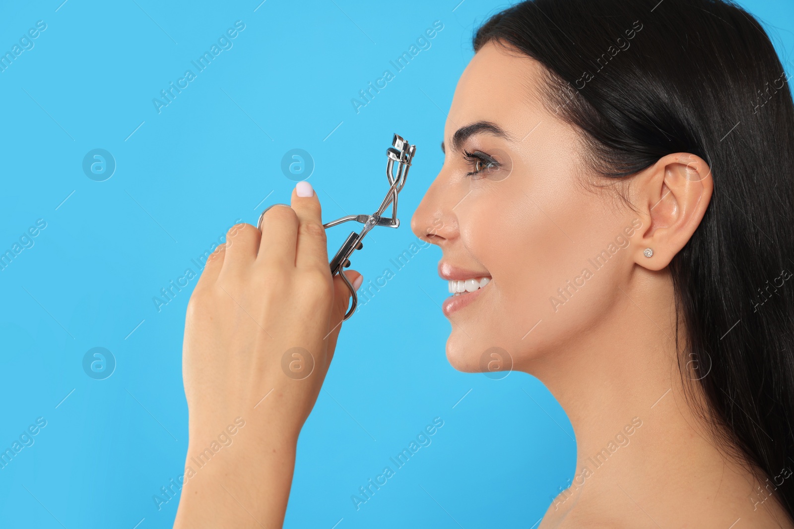 Photo of Beautiful young woman using eyelash curler on light blue background