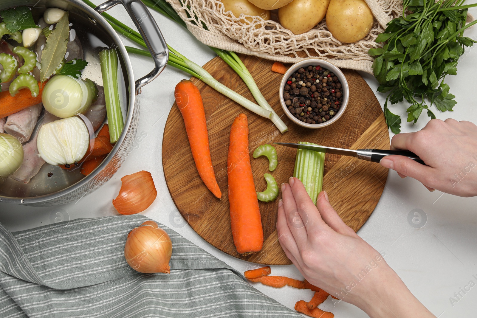 Photo of Cooking tasty bouillon. Woman cutting celery at white table, top view