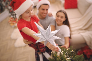 Photo of Family decorating Christmas tree indoors, focus on star topper