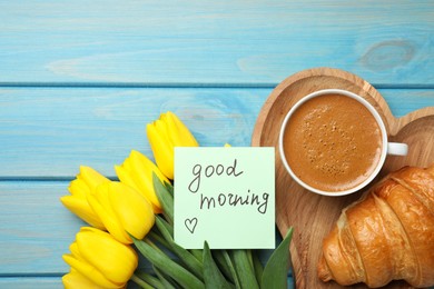 Photo of Cup of aromatic coffee with croissant, beautiful yellow tulips and Good Morning note on light blue wooden table, flat lay. Space for text