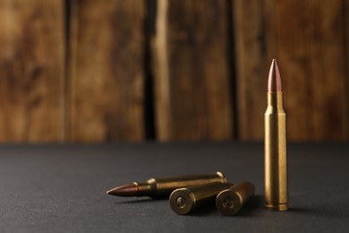 Photo of Bullets on black table against wooden background, closeup. Space for text