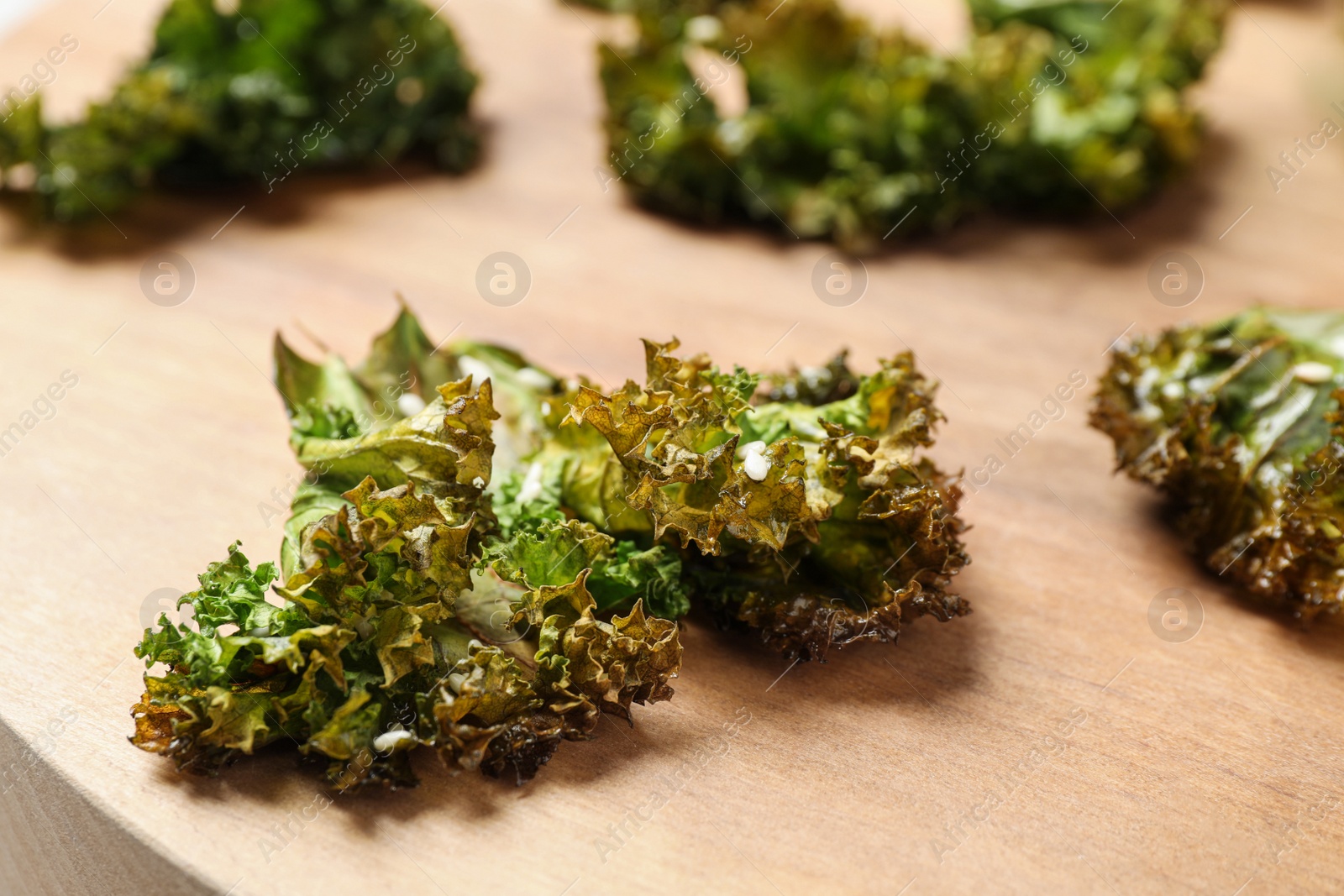 Photo of Tasty baked kale chips on wooden table, closeup