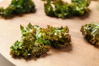 Tasty baked kale chips on wooden table, closeup