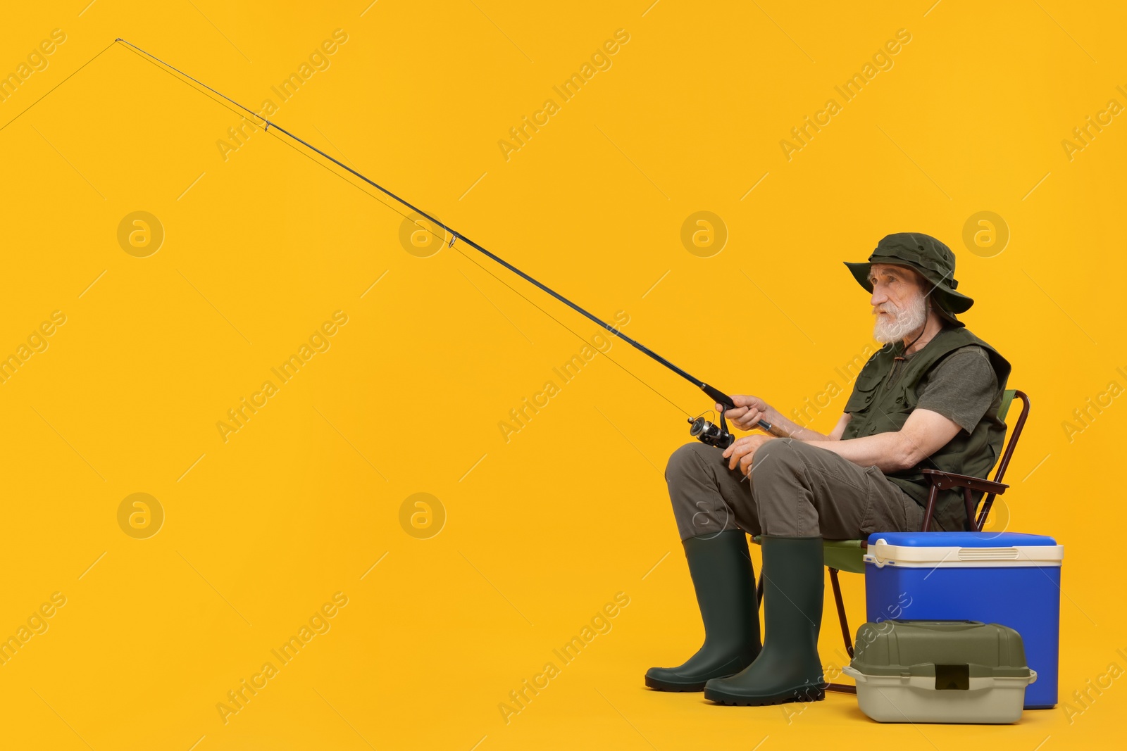 Photo of Fisherman with fishing rod on chair against yellow background, space for text