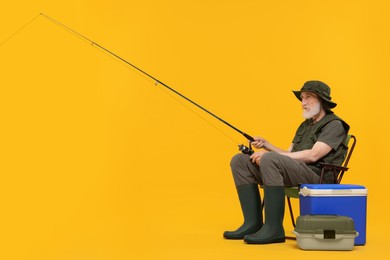 Fisherman with fishing rod on chair against yellow background, space for text