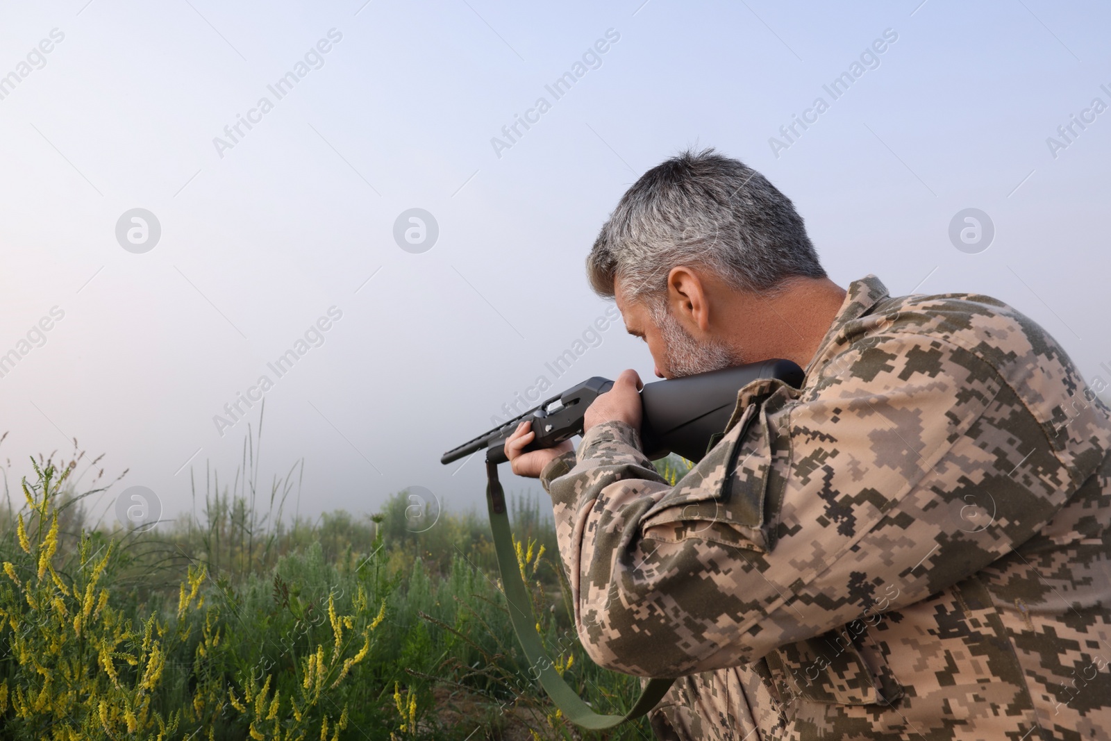 Photo of Man wearing camouflage and aiming with hunting rifle outdoors. Space for text