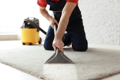 Photo of Male worker cleaning carpet with vacuum indoors