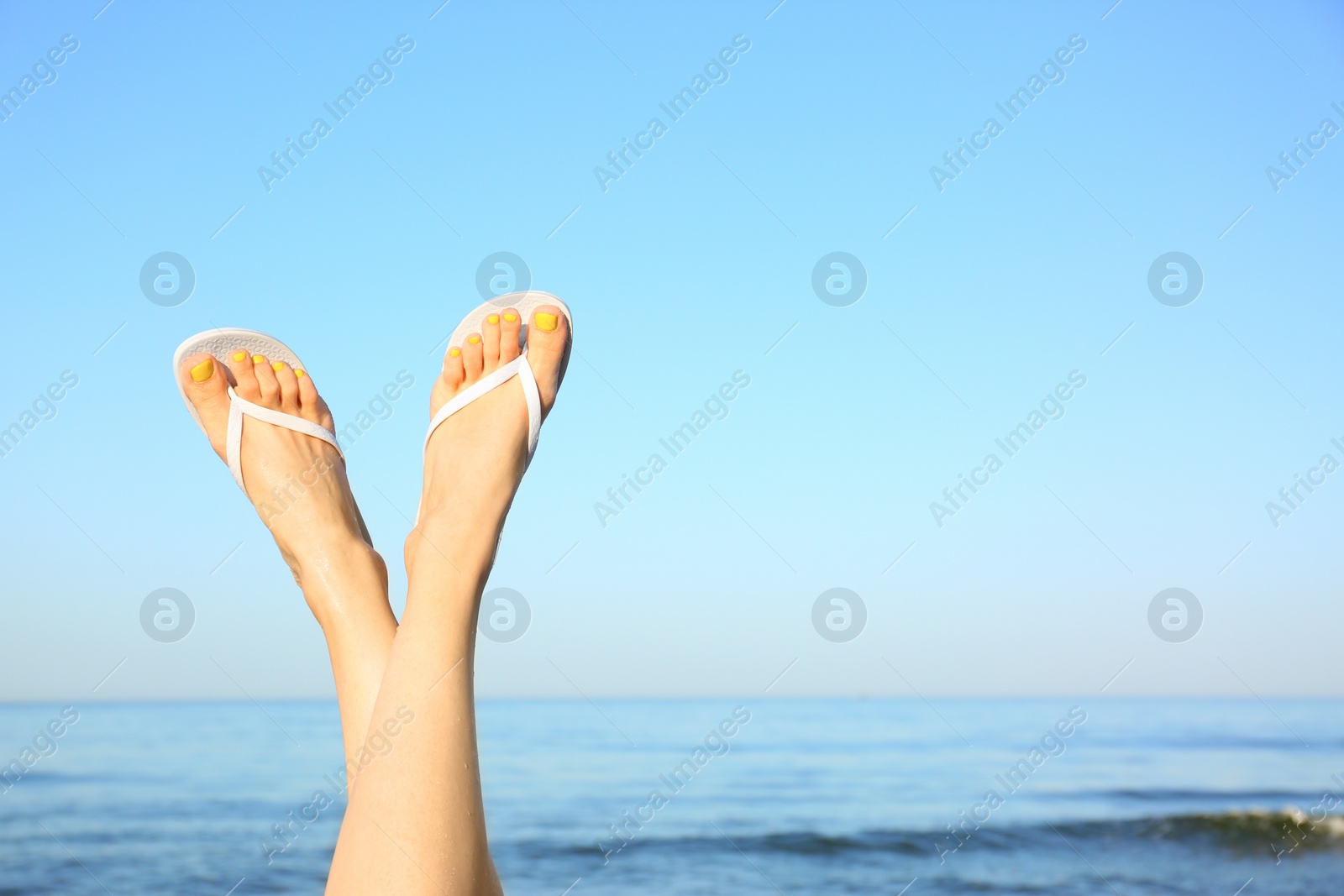 Photo of Closeup of woman wearing flip flops near sea, space for text. Beach accessories