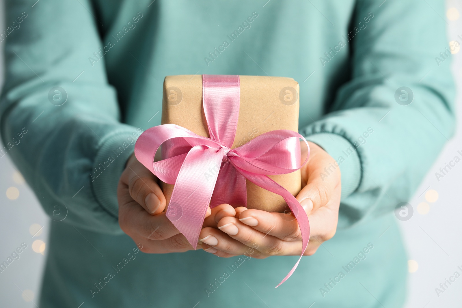 Photo of Woman holding gift box with pink bow on light grey background, closeup