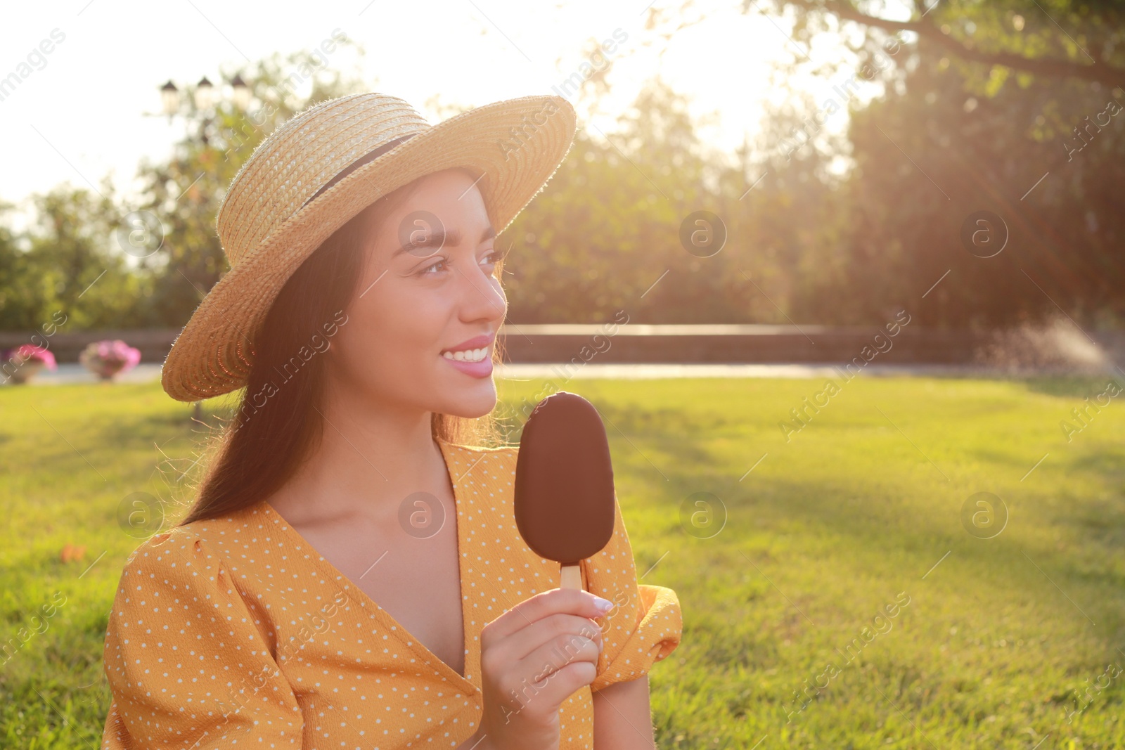 Photo of Beautiful young woman holding ice cream glazed in chocolate outdoors, space for text