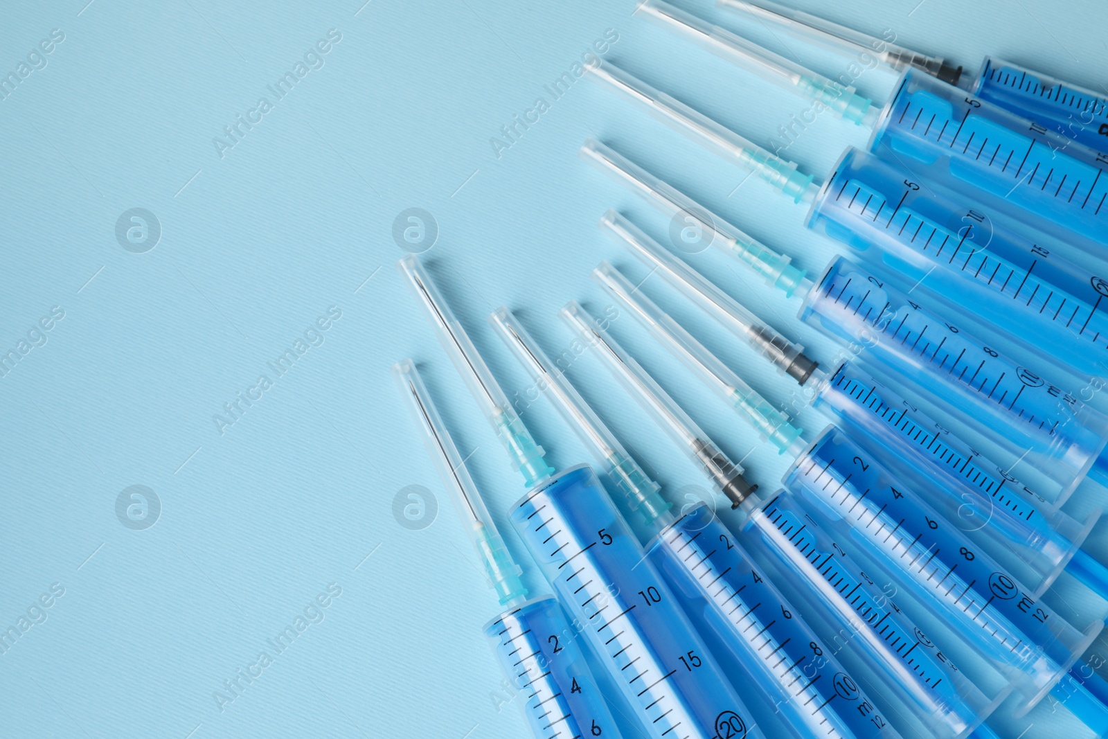 Photo of Disposable syringes with needles on light blue background, flat lay. Space for text