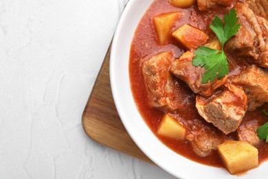 Delicious goulash in bowl on white textured table, top view. Space for text