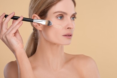 Photo of Woman applying foundation on face with brush against beige background