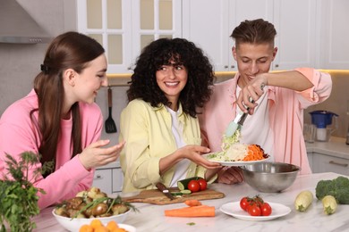 Photo of Friends cooking healthy vegetarian meal at white marble table in kitchen