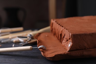 Photo of Clay and modeling tool on dark gray wooden table in workshop, closeup