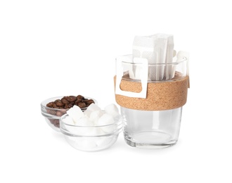 Photo of Glass cup with drip coffee bag, beans and sugar cubes isolated on white