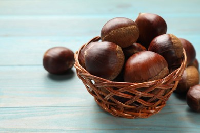 Wicker bowl with roasted edible sweet chestnuts on light blue wooden table, closeup. Space for text
