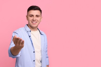 Photo of Handsome man inviting to come in against pink background. Space for text