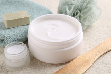 Photo of Body care cream in open jars on light textured table, closeup