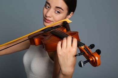 Beautiful woman playing violin on grey background, closeup